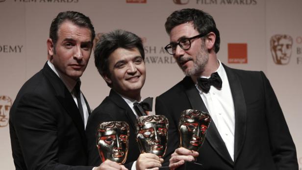 Drei Männer in Anzügen halten goldene BAFTA-Masken.