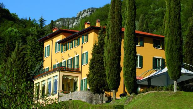 Ein gelbes Haus mit grünen Fensterläden steht inmitten einer grünen Landschaft.