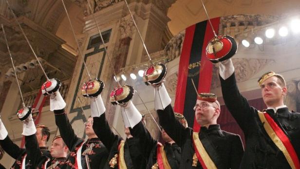 Studentenverbindungsmitglieder in traditioneller Kleidung halten Degen in die Luft.