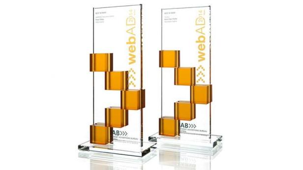 Zwei WebAd Awards 2014 aus transparentem Acrylglas mit goldenen Akzenten stehen auf einem Tisch.