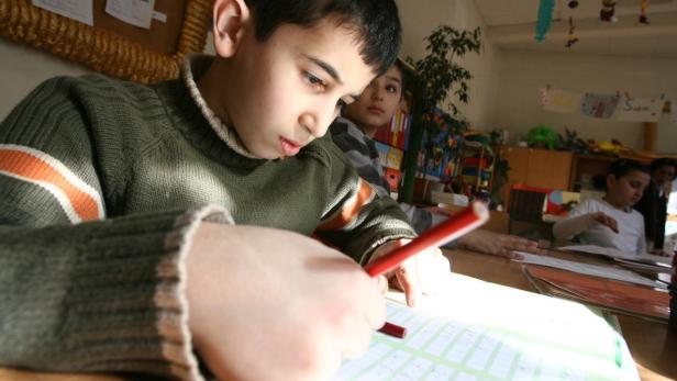 Ein Junge sitzt in einem Klassenzimmer und schreibt mit einem roten Stift.
