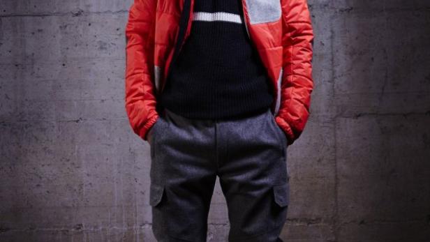 Ein Mann mit Skibrille und roter Jacke posiert vor einer Betonwand.