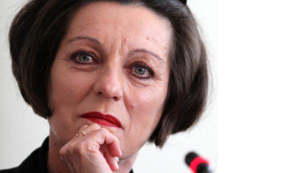 Eine Frau mit roten Lippenstift und dunklen Haaren denkt nach.