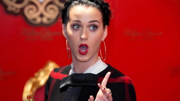 Katy Perry posiert mit offenem Mund vor einem roten Hintergrund.