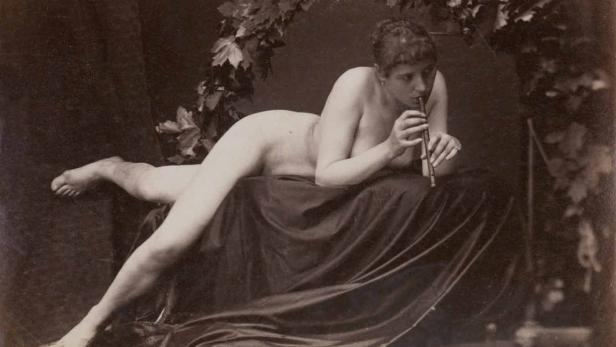 Eine nackte Frau liegt auf einem Tuch und spielt Flöte.