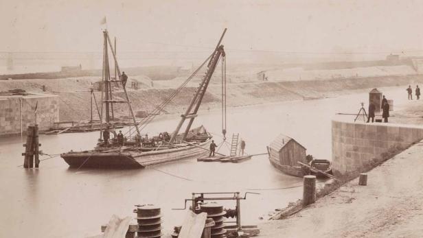 Historische Aufnahme von Bauarbeiten an einem Flussufer mit Schiffen und Arbeitern.