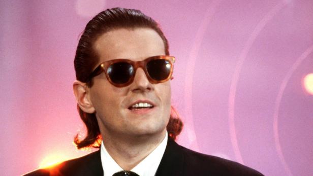 Thomas Anders von Modern Talking mit Sonnenbrille vor einem rosa Hintergrund.