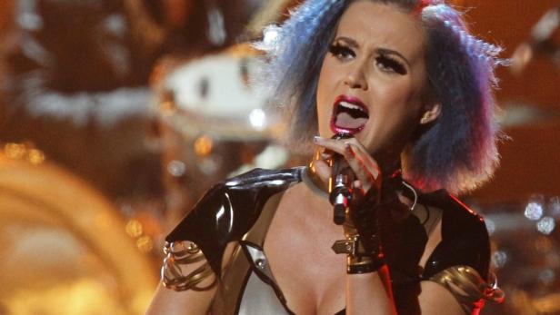 Katy Perry singt mit blau gefärbten Haaren auf einer Bühne in ein Mikrofon.
