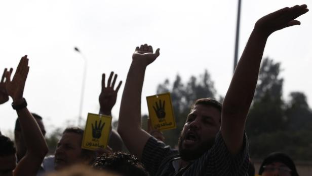 Eine Gruppe von Demonstranten hält Schilder mit einer Hand darauf und ruft Parolen.
