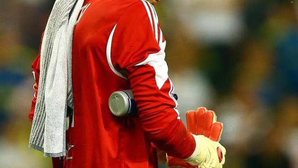 Ein Torwart in roter Sportkleidung hält seine Handschuhe in der Hand.