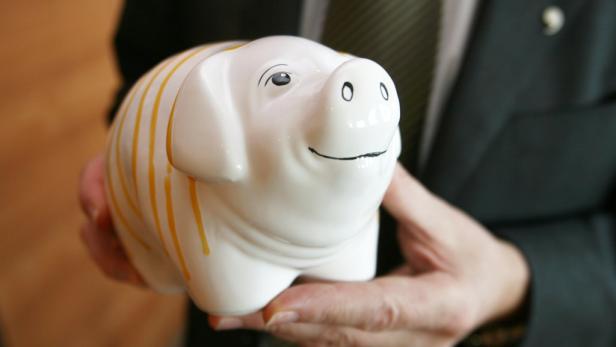 Eine Person hält ein weißes Sparschwein mit gelben Streifen in den Händen.