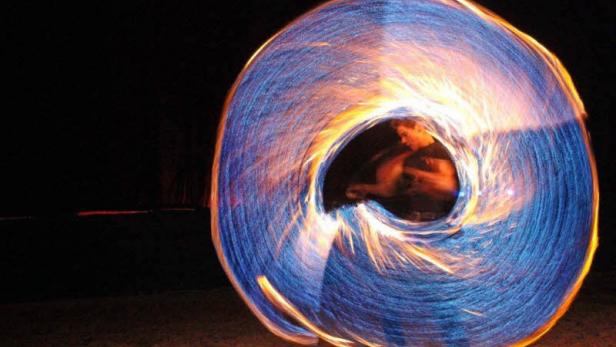 Ein Mann führt eine Feuershow mit brennenden Fackeln in der Dunkelheit auf.