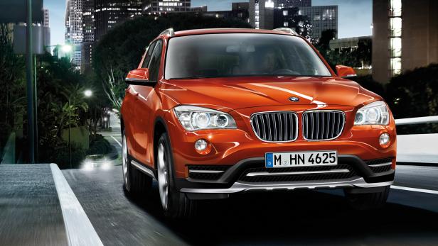Ein orangefarbener BMW X1 fährt auf einer Straße in einer Stadt bei Nacht.