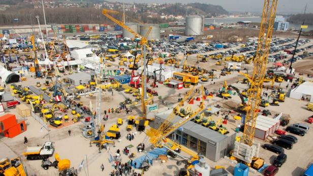 Eine Vogelperspektive auf eine Baumaschinenausstellung mit vielen Menschen und Baugeräten.