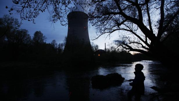 Ein Kind steht im Fluss vor einem Kühlturm im Abendlicht.