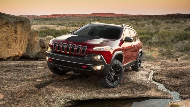 Ein roter Jeep Cherokee steht auf einem Felsen in einer hügeligen Landschaft.