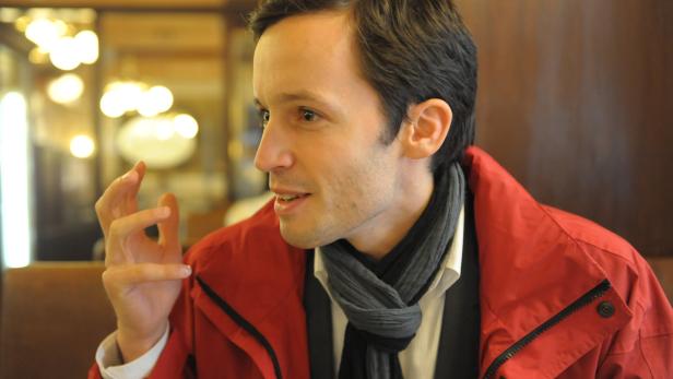 Ein Mann mit roter Jacke und Schal gestikuliert beim Sprechen.
