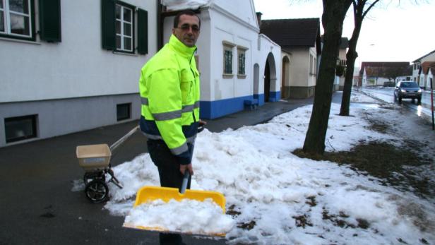 Ein Mann mit Warnweste schaufelt Schnee auf einer Straße.