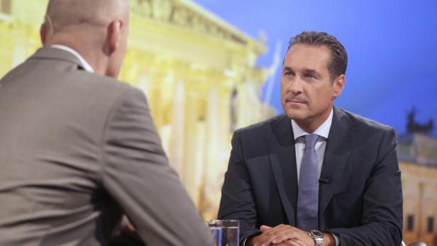 Ein Mann im Anzug sitzt in einem Fernsehstudio und spricht mit einer anderen Person.