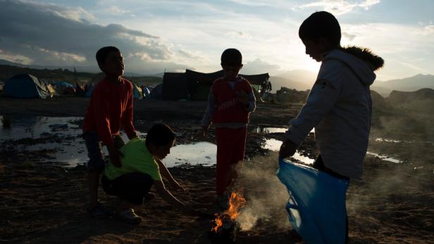 Vier Kinder machen ein kleines Lagerfeuer in einem Flüchtlingslager.
