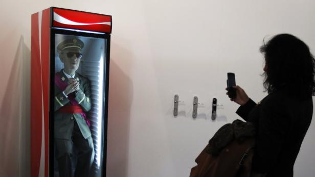 Eine Frau fotografiert eine Statue von Francisco Franco in einem Coca-Cola-Kühlschrank.