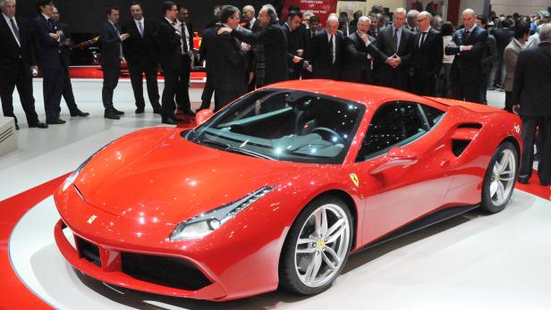 Ein roter Ferrari steht auf einer Automobilmesse, umringt von Menschen in Anzügen.