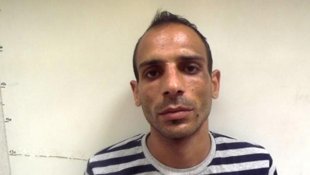 Ein Mann mit kurz geschnittenen, dunklen Haaren und einem gestreiften Hemd vor einer weißen Wand.