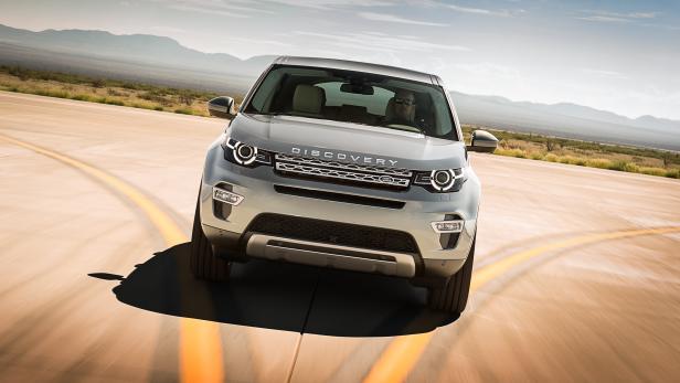 Ein silberner Land Rover Discovery fährt auf einer Landstraße.