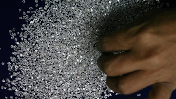 Eine Hand berührt eine große Menge ungeschliffener Diamanten.