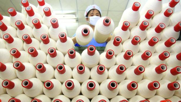 Eine Arbeiterin in einer Fabrik hantiert mit Garnrollen.