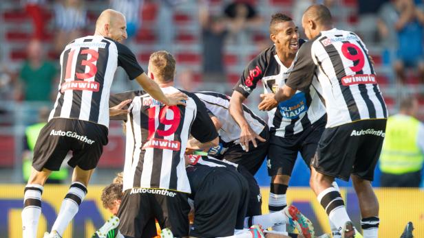 Fußballspieler in schwarz-weiß gestreiften Trikots feiern ein Tor.