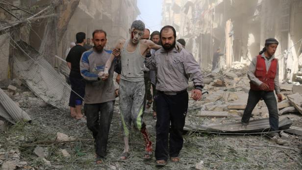 Männer tragen einen verletzten Jungen durch die Trümmer eines zerstörten Gebäudes.