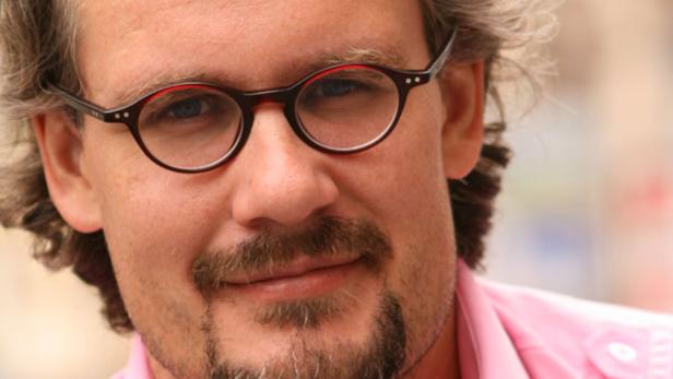 Porträt eines Mannes mit Brille und Bart in einem rosa Hemd.