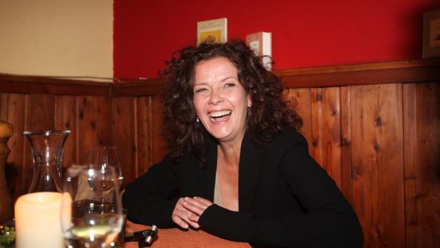Eine lachende Frau sitzt an einem Tisch in einem Restaurant.