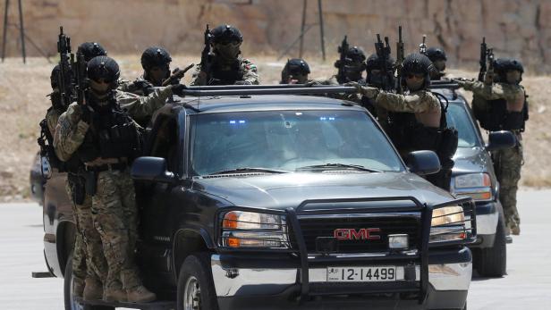 Bewaffnete Sicherheitskräfte stehen um zwei GMC-Trucks mit jordanischen Nummernschildern.