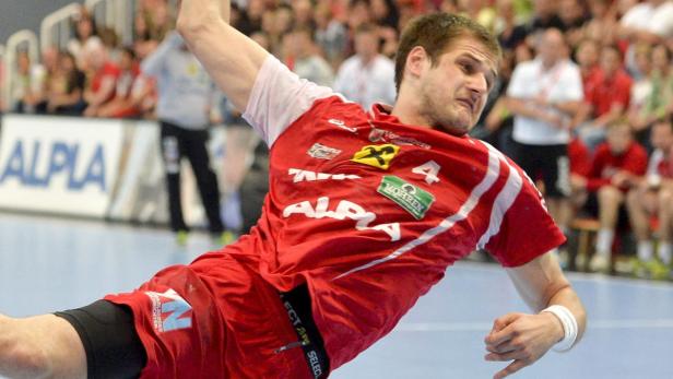 Ein Handballspieler in rotem Trikot wirft den Ball während eines Spiels.