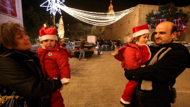 epa01584205 Palestinian children dressed up in Santa Claus outfits as they view the lights hung up in Manger Square in the West Bank town of Bethlehem on 23 December 2008. Behind is the Church of the Nativity, accepted as the traditional birth place of Jesus Christ. Tomorrow Bethlehem is expecting a huge increase in pilgrim coming to the town to take part in the festivities and the Christmas procession. EPA/YOSSI ZAMIR ISRAEL OUT