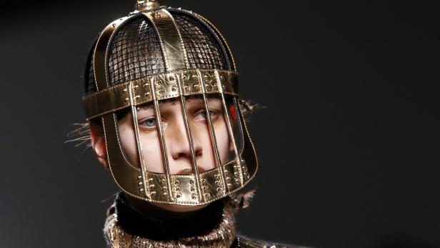 Ein Model trägt einen goldenen, käfigartigen Kopfschmuck mit Nieten.