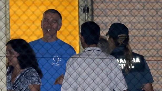 Ein Mann in blauem T-Shirt steht hinter einem Zaun, neben einer Frau und zwei weiteren Personen.