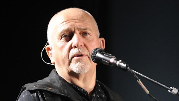 Peter Gabriel singt in ein Mikrofon auf einer Bühne.