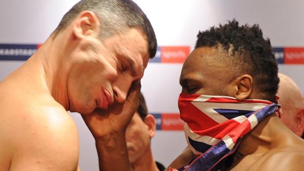 Zwei Boxer stehen sich bei einer Pressekonferenz gegenüber, einer mit einer Maske der britischen Flagge.