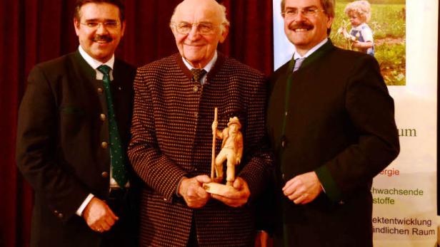 Drei Männer posieren mit einer Holzstatuette vor einem Agrar Plus Banner.