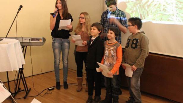 Eine Gruppe von Kindern und Jugendlichen steht auf einer Bühne und liest von Zetteln ab.