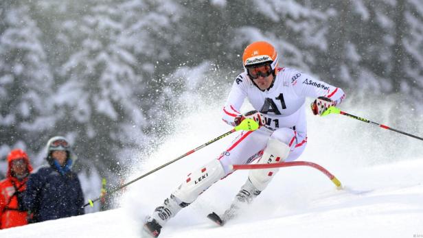Ein Skirennfahrer in weißer Rennkleidung und orangefarbenem Helm fährt einen Slalomkurs hinunter.