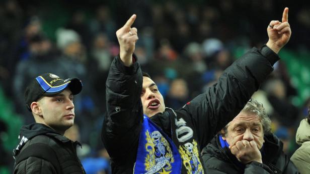 Ein Mann mit einem Schal und einer Jacke gestikuliert in einem Fußballstadion.