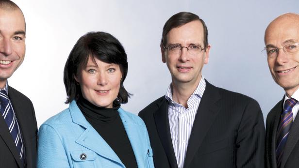 Vier Personen in Anzügen und formeller Kleidung lächeln in die Kamera.