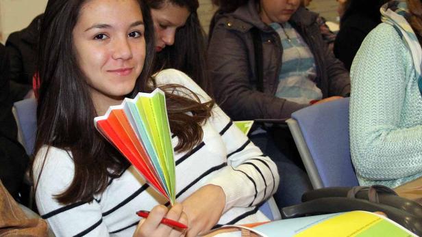 Ein junges Mädchen sitzt mit einem bunten Fächer und einem Stift in der Hand.