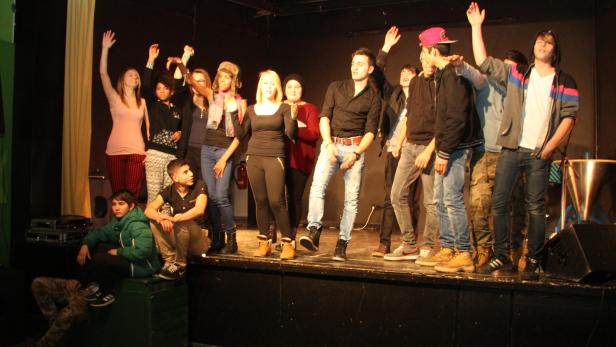 Eine Gruppe junger Leute steht auf einer Bühne und winkt ins Publikum.