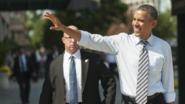 Barack Obama winkt, während ein Sicherheitsbeamter im Hintergrund steht.