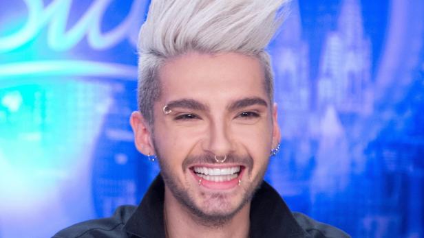 Porträt von Bill Kaulitz mit blonden Haaren und Piercings, der lächelt.